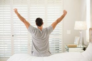 Man waking up refreshed. Sitting on edge of bed stretching arms out.