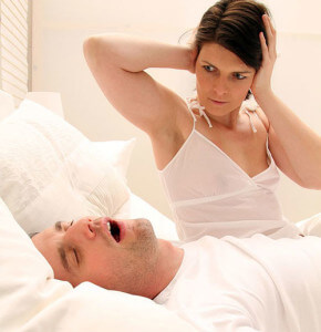 Woman holding ears with man snoring 