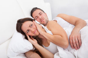 Woman covering ears laying next to snoring man