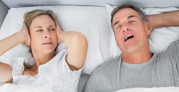 man snoring in bed next to woman 