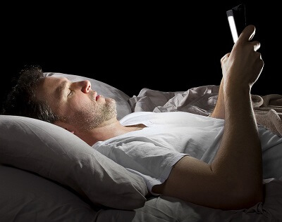 Man laying in bed looking at smart phone in dark