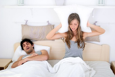 Couple in bed guy snoring woman covering ears with pillow